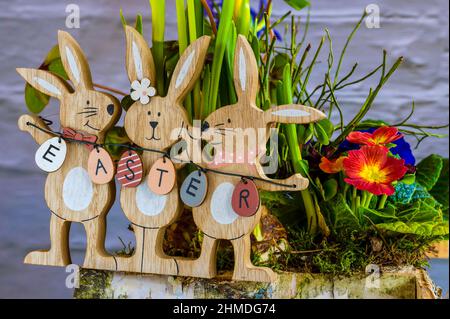 Flower arrangement with wooden Easter bunnies as decoration and the text Easter on the Easter eggs. Stock Photo