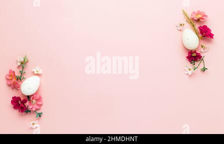 Easter holiday pink mockup background. Top view from above to white Easter eggs, different colorful flowers, frame border. Card with copy space to place text. Minimal flat lay. High quality photo Stock Photo