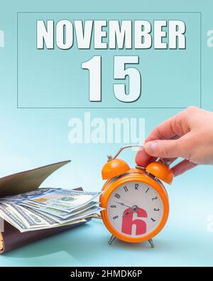 November 15th. Hand holding an orange alarm clock, a wallet with cash and a calendar date. Day 15 of month. Business planning. Time is money. Tax time Stock Photo