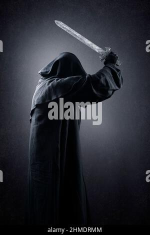 Warrior with hooded cape and medieval sword over dark misty background Stock Photo