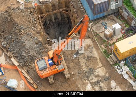 Excavator at a construction site while digging trenches for calcining sewer and drainpipes with a raised bucket, top aerial view Stock Photo