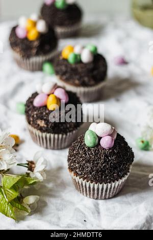 Homemade Easter chocolate cupcakes with chocolate butter cream frosting and candy eggs. Easter brunch. spring blossom decoration. on white linen table Stock Photo