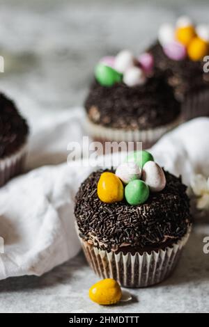 Homemade Easter chocolate cupcakes with chocolate butter cream frosting and candy eggs. Easter brunch. spring blossom decoration. on white linen table Stock Photo