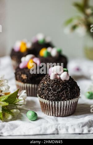 Homemade Easter chocolate cupcakes with chocolate butter cream frosting and candy eggs. Easter brunch. spring blossom decoration. on white linen table Stock Photo