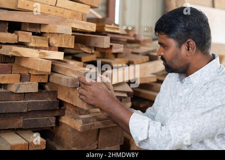 Focus on hand, Back view of carpenter selecting or searching best wood for making furniture at workshop - concept of quality assurance, small business Stock Photo
