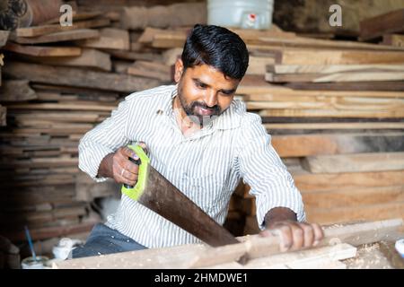 Indian carpenter manually cutting wood using sawing equipment - concept of Hard working, woodworker and craftsman and skilled labour. Stock Photo