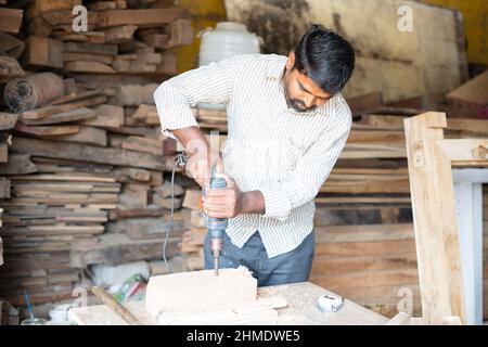 carpenter drilling wood using machine at workshop - concept of craftperson, skilled profession and workshop. Stock Photo