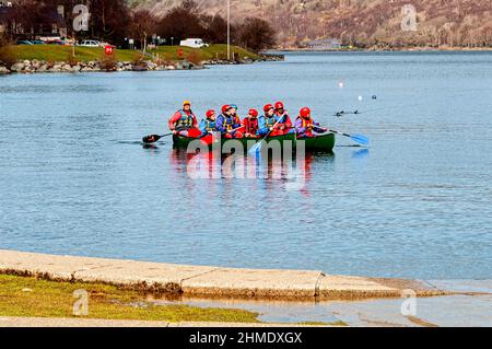 Trainees dressed in appropriate safety gear i.e. helmets and life jackets learn how to paddle a canoe on the panoramic freshwater Padarn lake Stock Photo