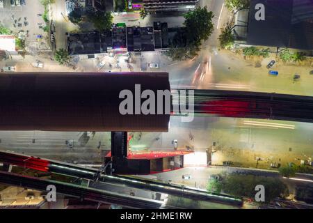 top down flat aerial shot showing red roof of elevated metro train station with track coming out over busy street with cars in bangalore gurgaon india Stock Photo