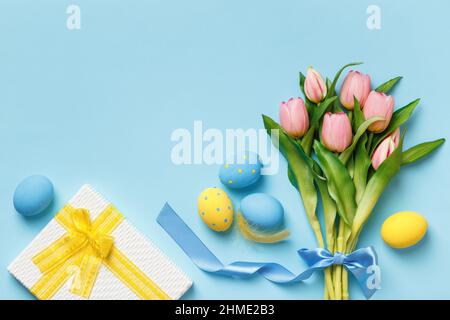 Easter eggs pink tulips gift on a blue background. Flat lay copy space top view. Stock Photo