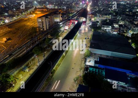 aerial drone shot showing elevated metro train station and tracks over busy street with light trails from traffic and cityscape in gurgaon, jaipur Stock Photo