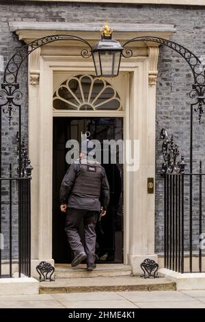 Police officer entering the famous black door at Number 10 Downing Street, London, UK Stock Photo