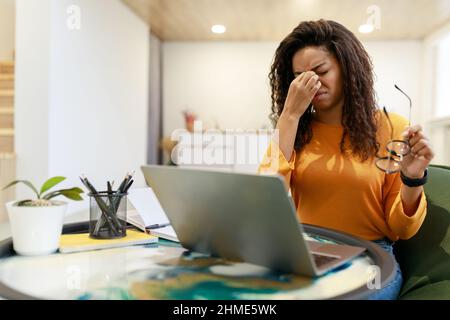 Tired black female worker sitting at desk with pc Stock Photo