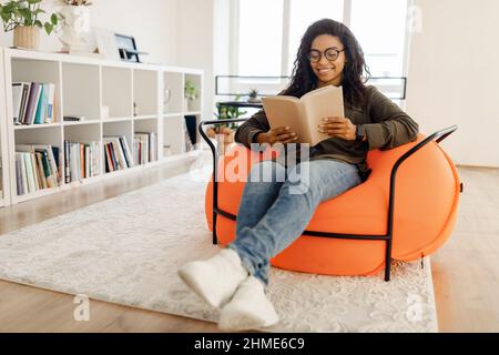 Smiling black woman in eyeglasses reading book Stock Photo