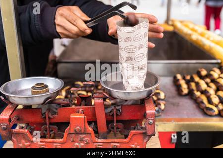 Istanbul, Turkey – Nov 19, 2021: street vendor weighing roasted chestnuts on balance scales before selling. Roasting chestnuts is a popular turkish st Stock Photo