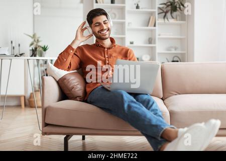 Smiling Arab man using pc at home, listening to music Stock Photo