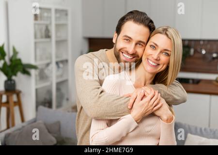 Harmonic relationships. Happy married couple posing for a photo on kitchen. Caucasian husband hugging his wife from behind. Happiest hearts make the happiest homes concept Stock Photo