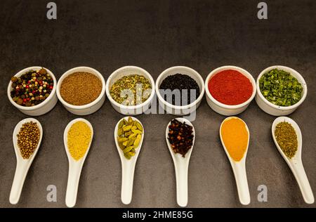 Seasonings of different varieties, in white bowls and spoons, on a gray background. Stock Photo
