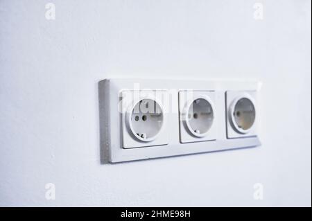 modern electrical sockets on a white wall. Close-up of a triple rosette. Stock Photo