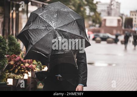 A man with a black wet umbrella was caught in a gust of wind on the street of the old city. Stock Photo