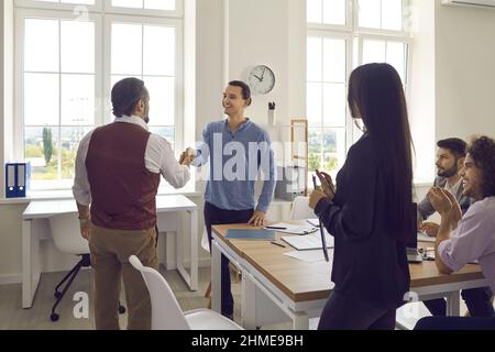 Business manager shakes hands with a young cheerful man, welcoming him as a new team member. Stock Photo