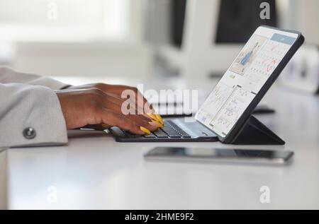 Black woman sitting at desk in office and typing on keyboard of her tablet computer Stock Photo