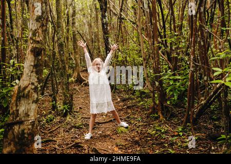 A little girl in a white dress walks through the jungle on a tropical island. Stock Photo