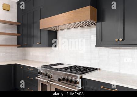 A luxury kitchen with black cabinets, granite counter top, tiled backsplash, stainless steel appliances, and gold hardware. Stock Photo