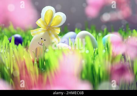 Easter eggs as cute bunnies on green grass against pink background. Holiday concept. Stock Photo