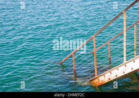 Old metal staircase goes down into the water - concept image with copy space. Stock Photo