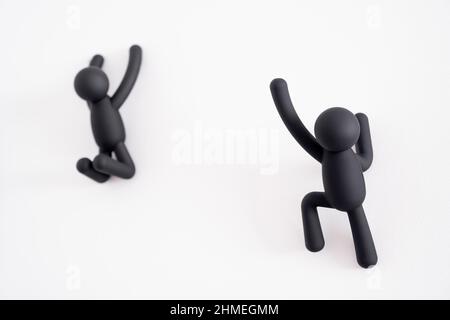 2 black 3D puppets climbing over a white background, human character , person hanging from a white wall, one trying to help the other that is out of f Stock Photo