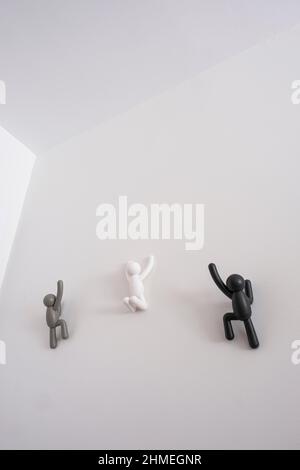 3 black grey and white 3D puppets climbing over a white wall, concept of self improvement, help each other, message of equality and non discrimination Stock Photo