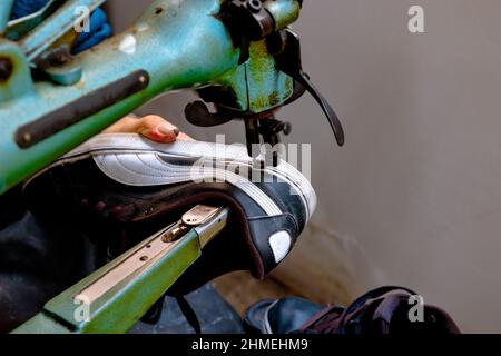 Sneaker repairing. Shoemaker repairs a sneaker on sewing machine. Selective focus. Noise included. Stock Photo