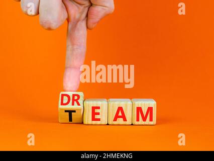 Dream team dreamteam symbol. Businessman turns wooden cubes and changes the word Dream to Team. Beautiful orange table orange background. Business and Stock Photo