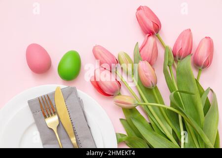 Easter place setting. Pastel color egg and tulip flower decoration on pink background, view from above. Spring Holiday celebration. Stock Photo