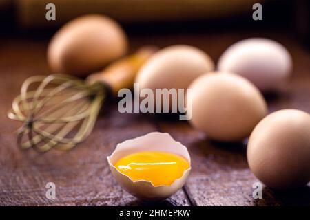 broken country chicken egg, visible yolk on wooden table, cooking with organic eggs Stock Photo