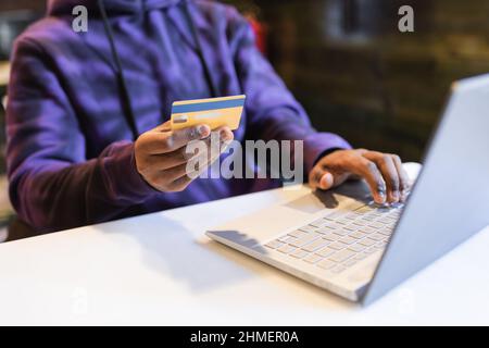 Crop anonymous African American male typing bank card data for online paying for online purchases in Internet in cafe Stock Photo
