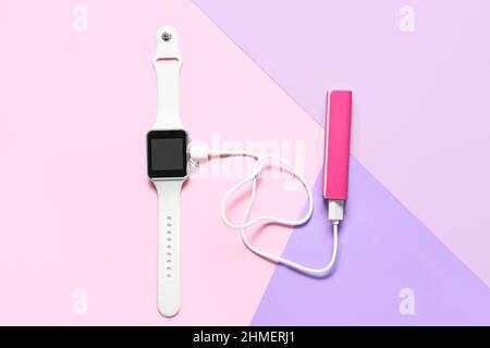 Pink power bank with smartwatch on color background Stock Photo