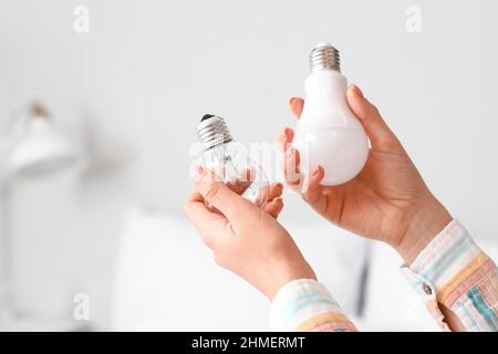 Woman holding different light bulbs in bedroom, closeup Stock Photo