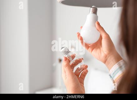 Woman holding different light bulbs in bedroom, closeup Stock Photo