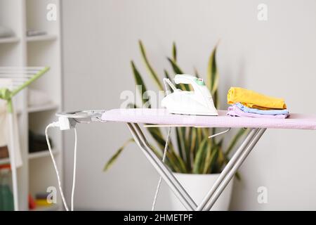 Electric iron and stack of clothes on board Stock Photo