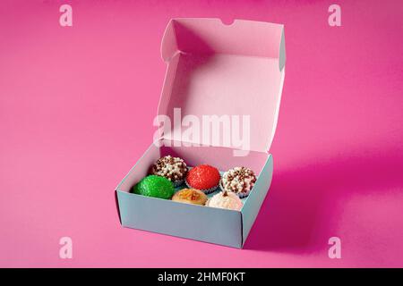 Candies of various flavors in a blue paper box. Pink background. Stock Photo