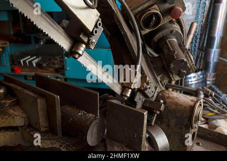 A metal band saw in the workshop cuts a metal rod with a liquid refrigerant. Gear blade of the machine. Stock Photo