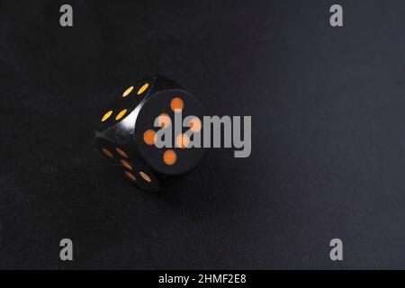 A black dice standing in balance on an edge and showing 6 on a black table. Stock Photo