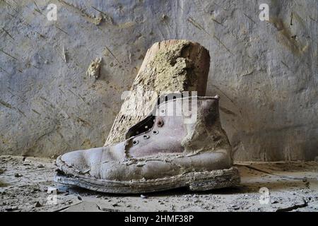 Ailing leather work boot stands on a wall, rotten shoe, shoe wreck ...
