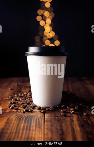 Paper cup of takeaway coffee with coffee beans on rustic wooden table and bokeh lights on background, Close up Stock Photo