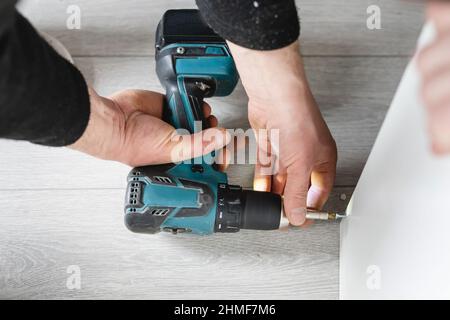 One unknown man caucasian male using electric cordless screwdriver drill assembling furniture at home DIY carpenter at work close up on hands copy spa Stock Photo