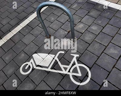 Parking for cargo bikes. A symbol painted on the sidewalk shows a cargo bike next to a mounting bracket. Hanover, Germany, February 5, 2022   ---  Parkplatz für Lastenräder. Ein auf den Bürgersteig gemaltes Symbol zeigt ein Lastenfahrrad neben einem Befestigungsbügel. Hannover, 5.2.2022 Stock Photo