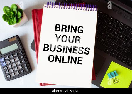 BRING YOUR BUSINESS ONLINE text on notebook with office supplies on the white background. Stock Photo