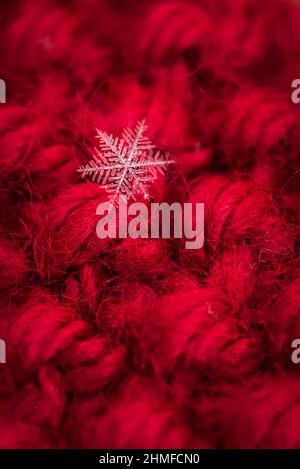 Macro close up of single snowflake against red wool background. Stock Photo